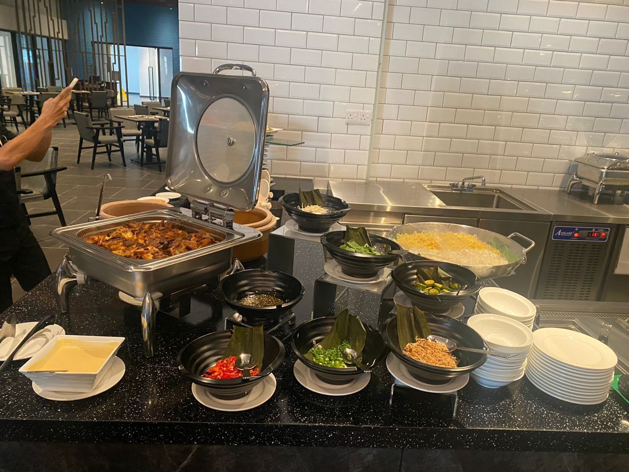 A buffet setup with various food items and a person serving.