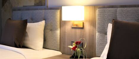 Una habitación de hotel con dos camas, una mesita de noche con lámpara y un jarrón con flores.