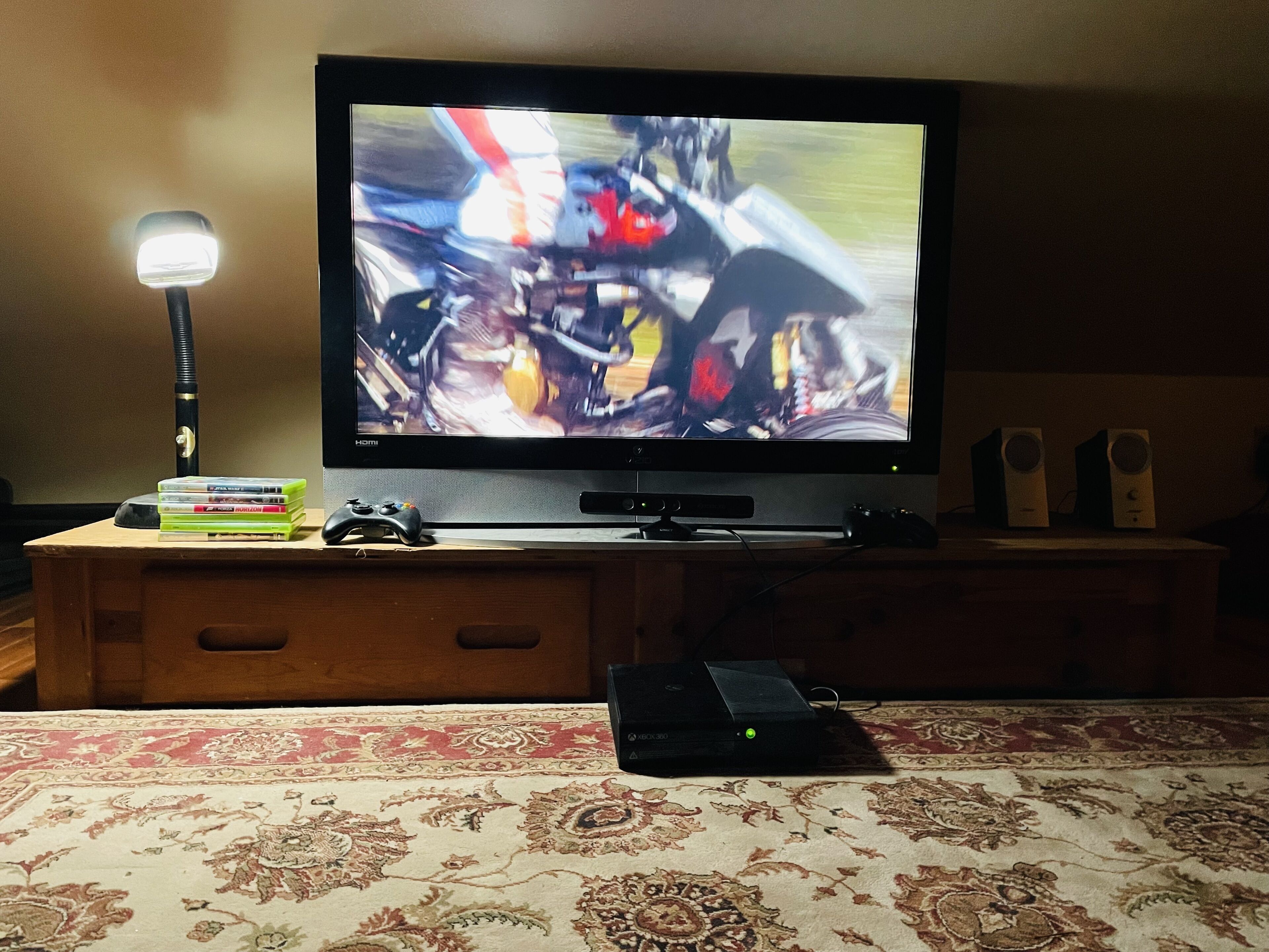 Un téléviseur posé sur un meuble en bois, avec une console de jeux vidéo et une lampe à côté.