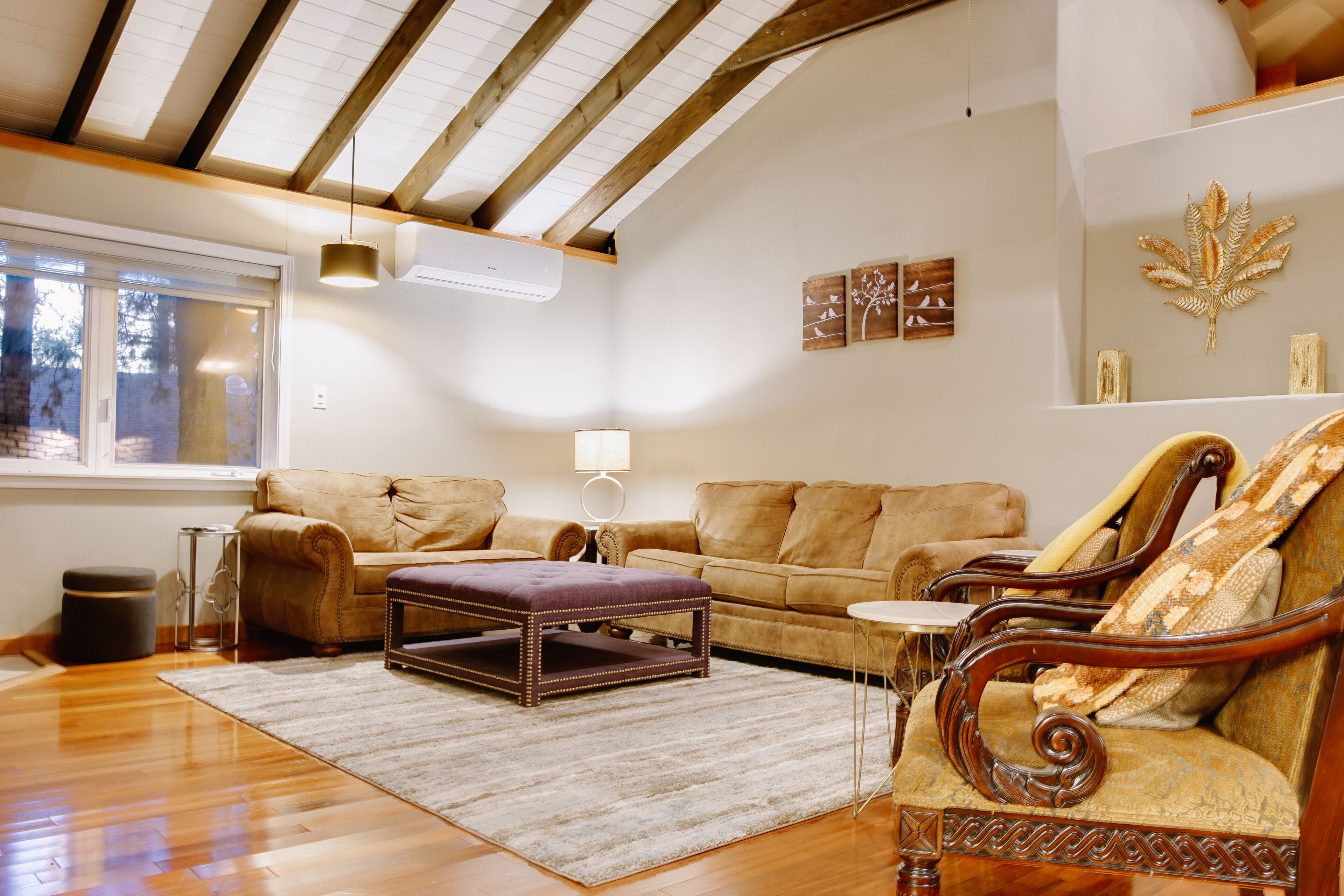 Un salón amplio con pisos de madera, un ventanal grande y un techo con vigas a la vista.