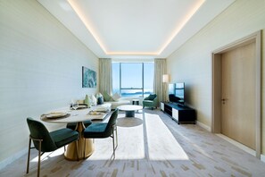 A modern hotel room with a dining area, seating, a television, and a view of the sea. - Maison Privee - Luxury Apt w/ Fabulous Views over Palm Jumeirah (Dubai)