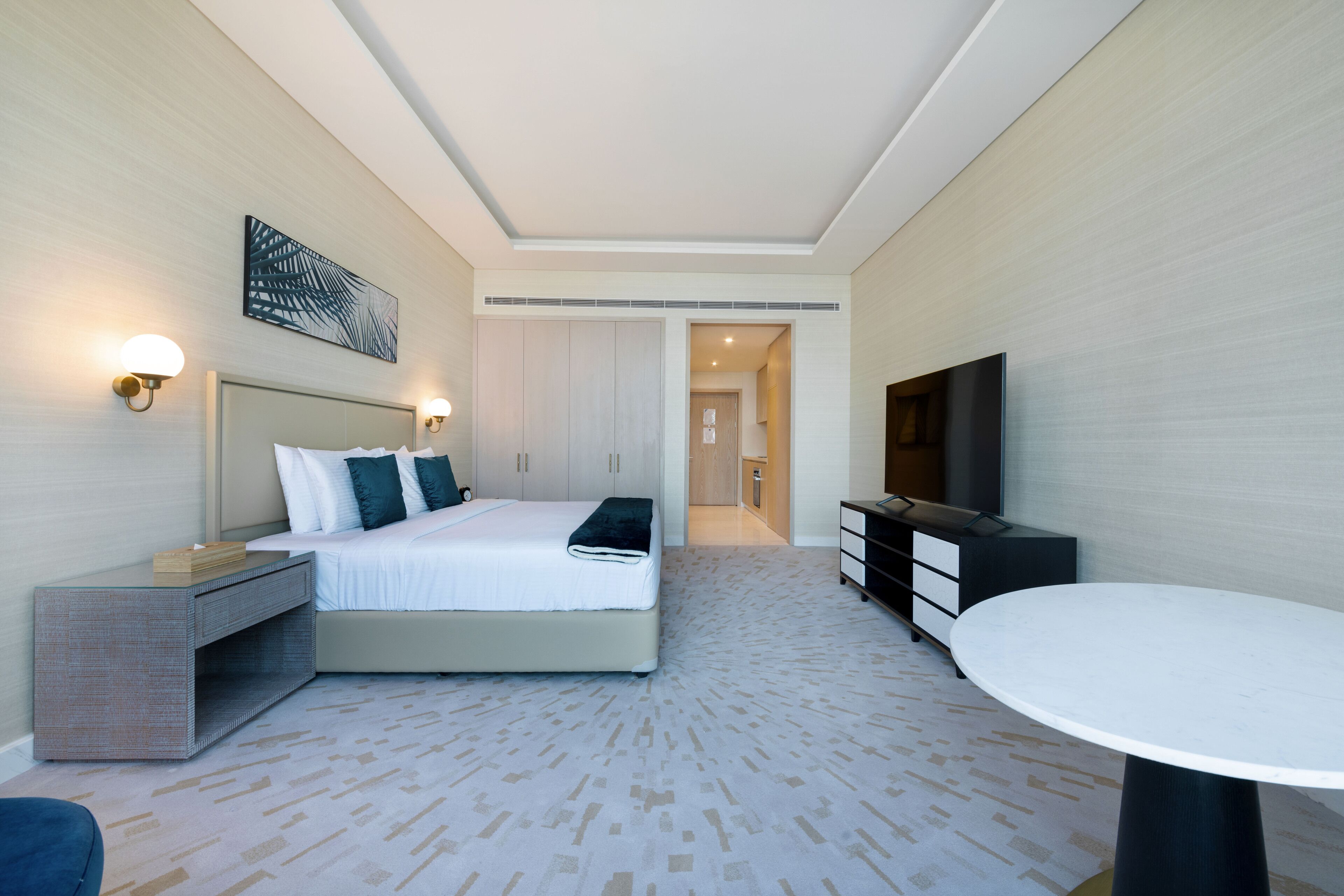 A modern hotel room with a bed, bedside tables, a TV, and a dining table.