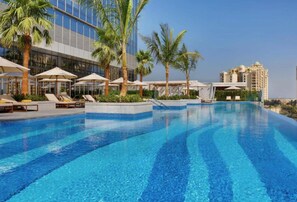 A swimming pool with lounge chairs and umbrellas, surrounded by palm trees and modern buildings. - Maison Privee - Luxury Apt w/ Fabulous Views over Palm Jumeirah (Dubai)