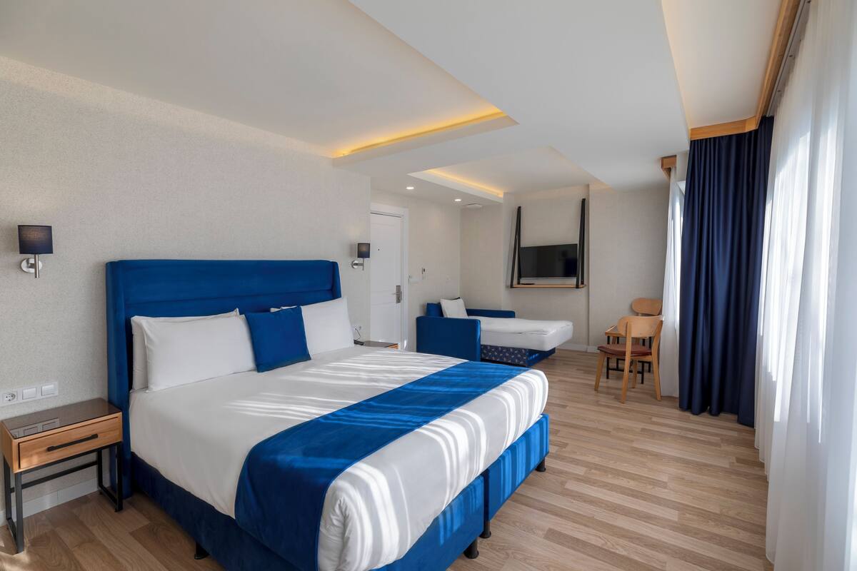 A hotel room with a large bed, bedside tables, a desk, a chair, and a TV.