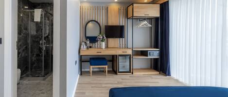 A modern hotel room with a shower, a desk with a chair, a bed, a TV, and a wardrobe.