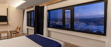 A modern hotel room with a large bed, a desk, and a TV.