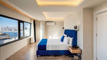 Una habitación de hotel moderna con una cama grande, un escritorio y vistas a un paisaje urbano a través de amplios ventanales.