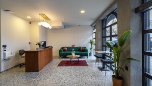 Un interior moderno con mostrador de recepción, sofá verde, mesa de centro y plantas en macetas.