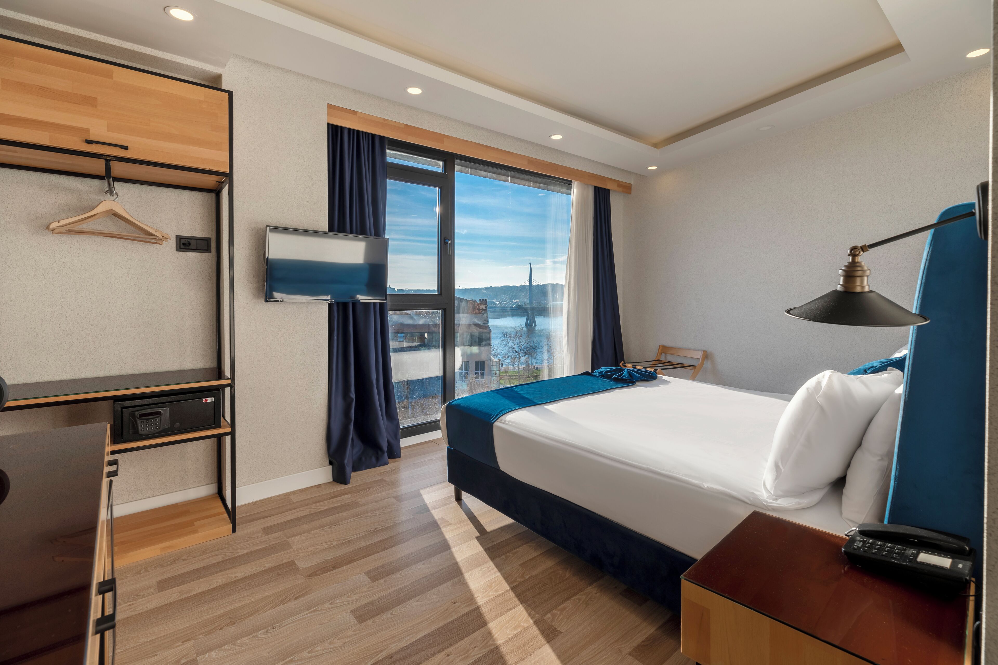 A hotel room with a bed, a desk, a TV, and a view of a cityscape.
