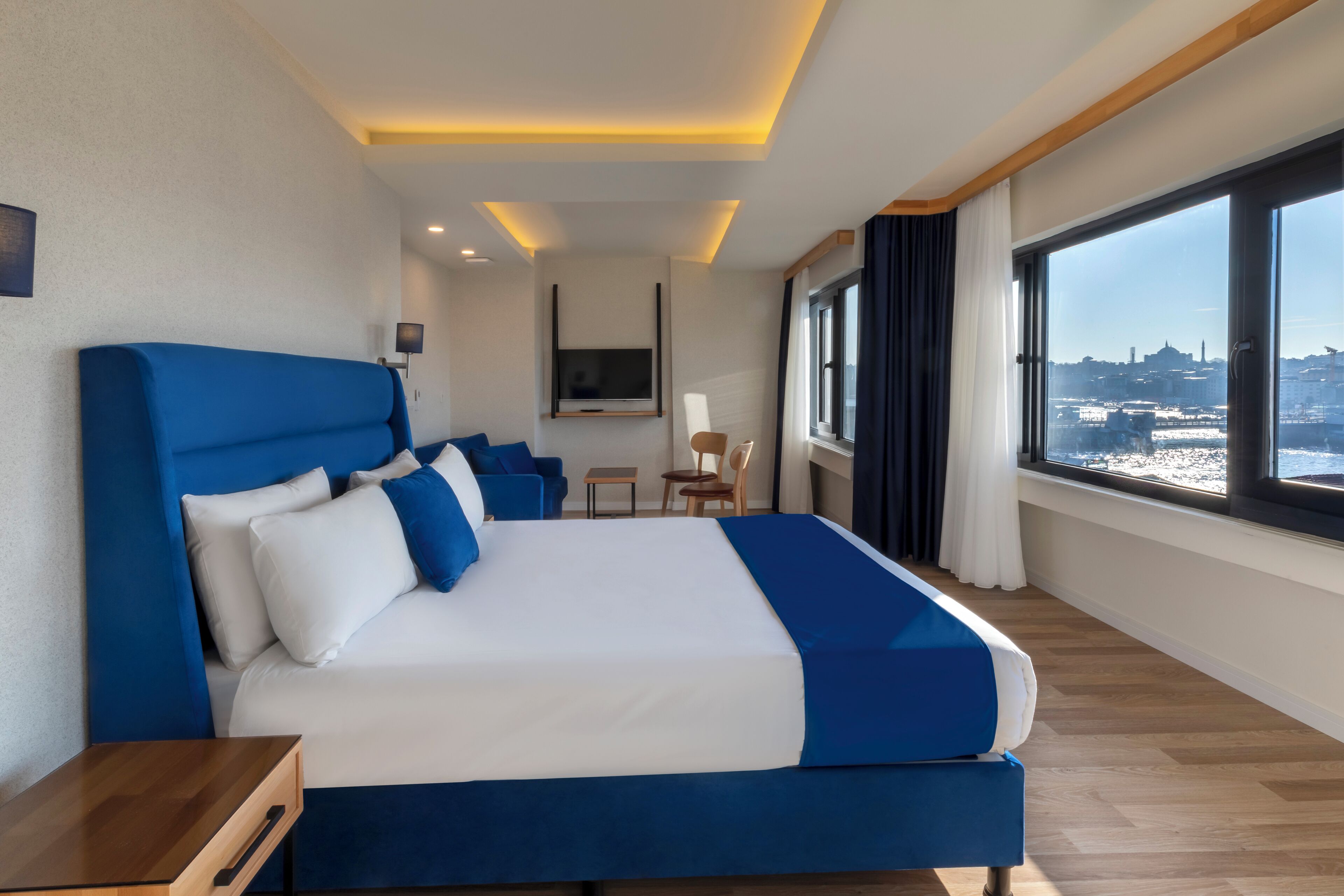 A modern hotel room with a large bed, a TV, and a city view.