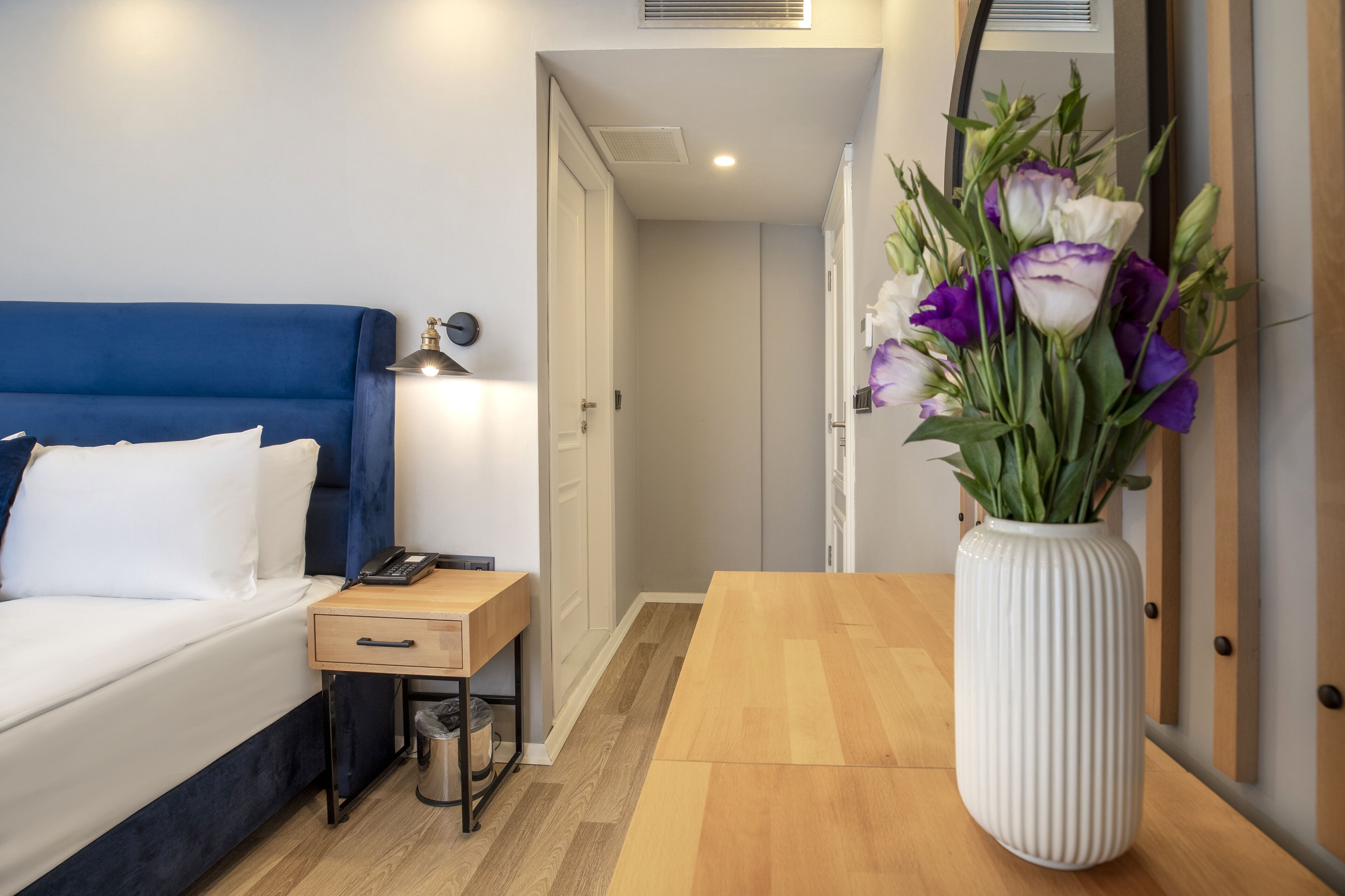 Habitació d'hotel amb un llit, una taula de nit, una làmpada i un vas amb flors.