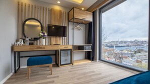 Un dormitorio moderno con un ventanal grande, un escritorio, un banco, un televisor y un armario.