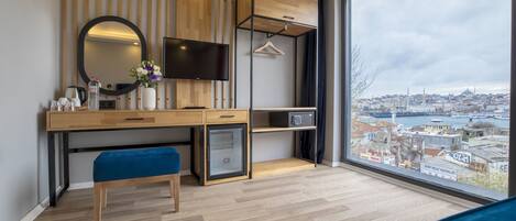 Quarto moderno com uma janela grande, uma escrivaninha, um banco, uma TV e um guarda-roupa.