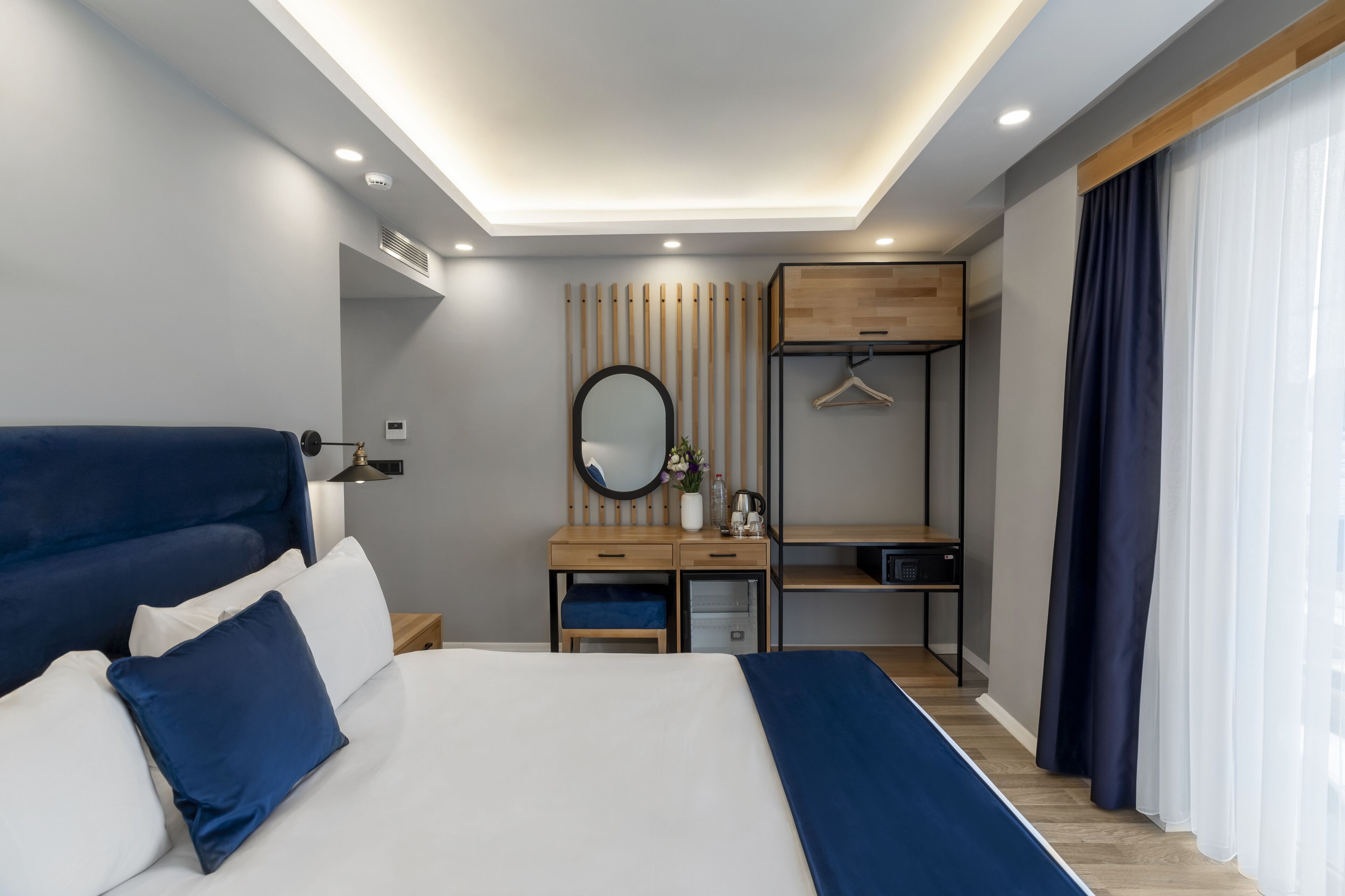 Una habitación de hotel moderna con una cama grande, una mesita de noche y un escritorio con un espejo y perchero.