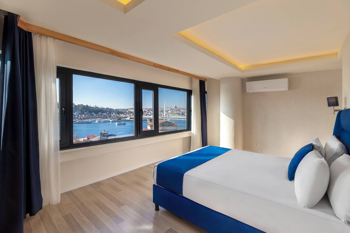 A hotel room with a large window offering a view of a cityscape and water.