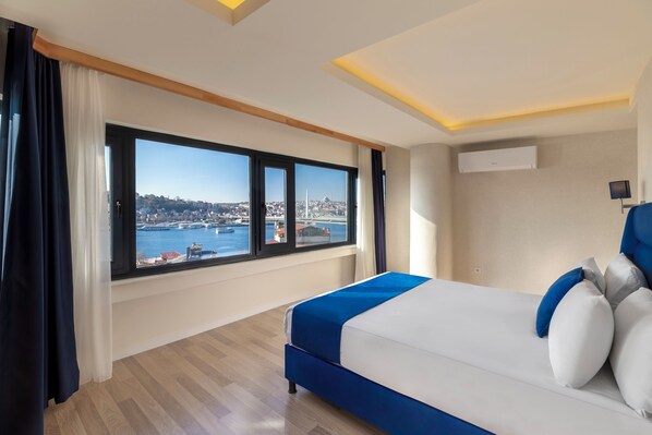 A hotel room with a large window offering a view of a cityscape and water.