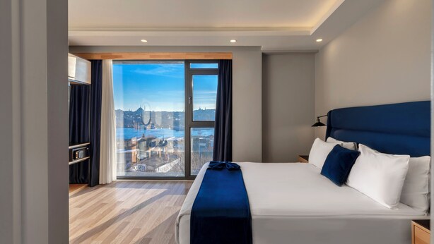 Habitación de hotel moderna con una cama grande, vistas a un paisaje urbano y suelo de madera.