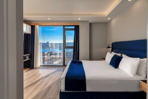 Moderni hotellihuone, jossa on suuri sänky, näkymä kaupunkimaisemaan ja puulattia.