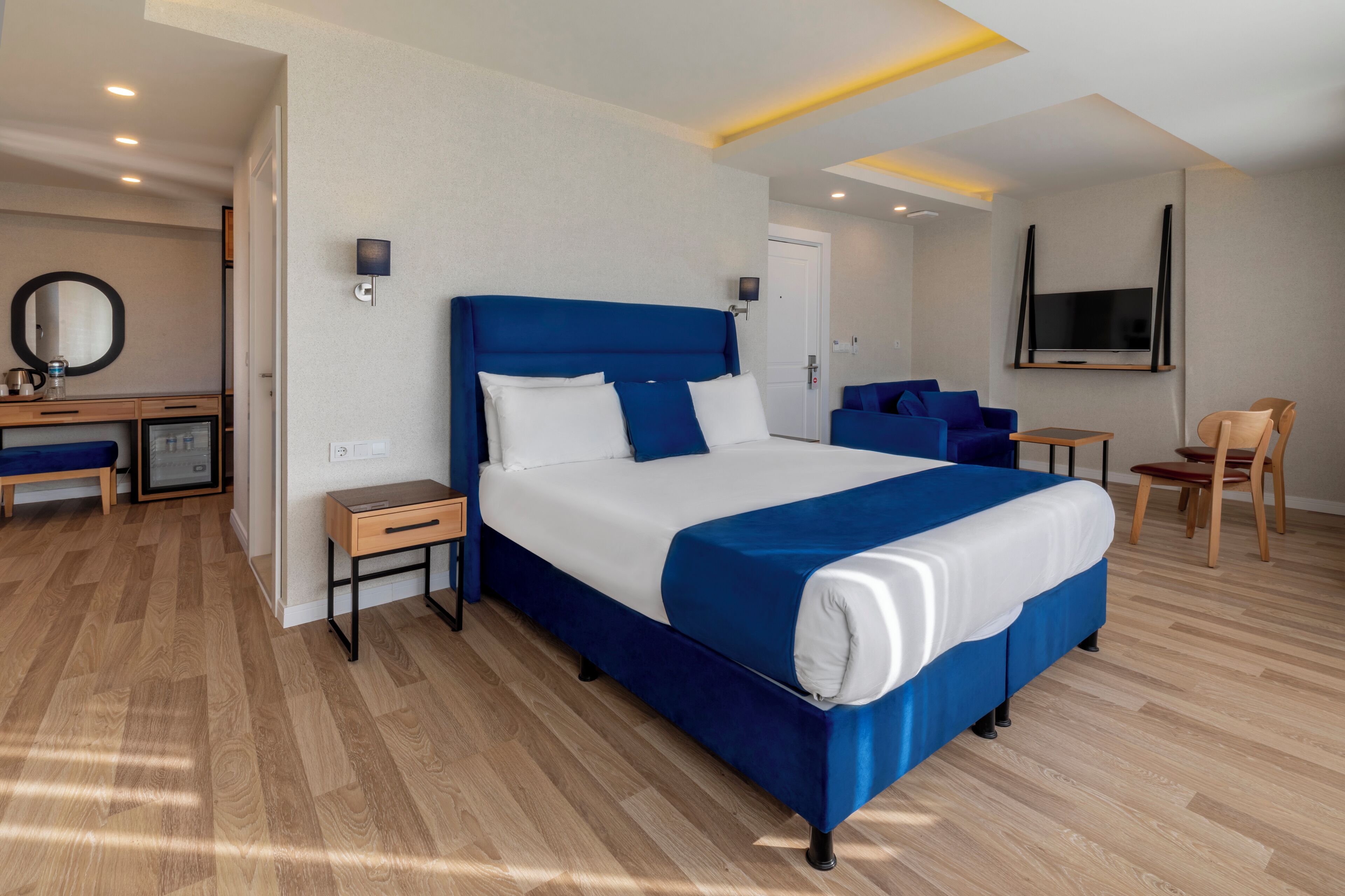Una habitación de hotel moderna con una cama grande, un escritorio con computadora, una silla y un televisor montado en la pared.