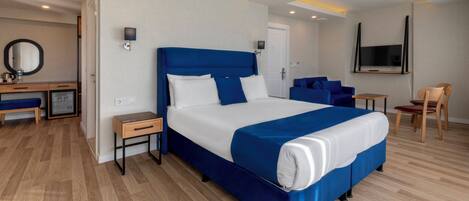 Una habitación de hotel moderna con una cama grande, un escritorio con computadora, una silla y un televisor montado en la pared.