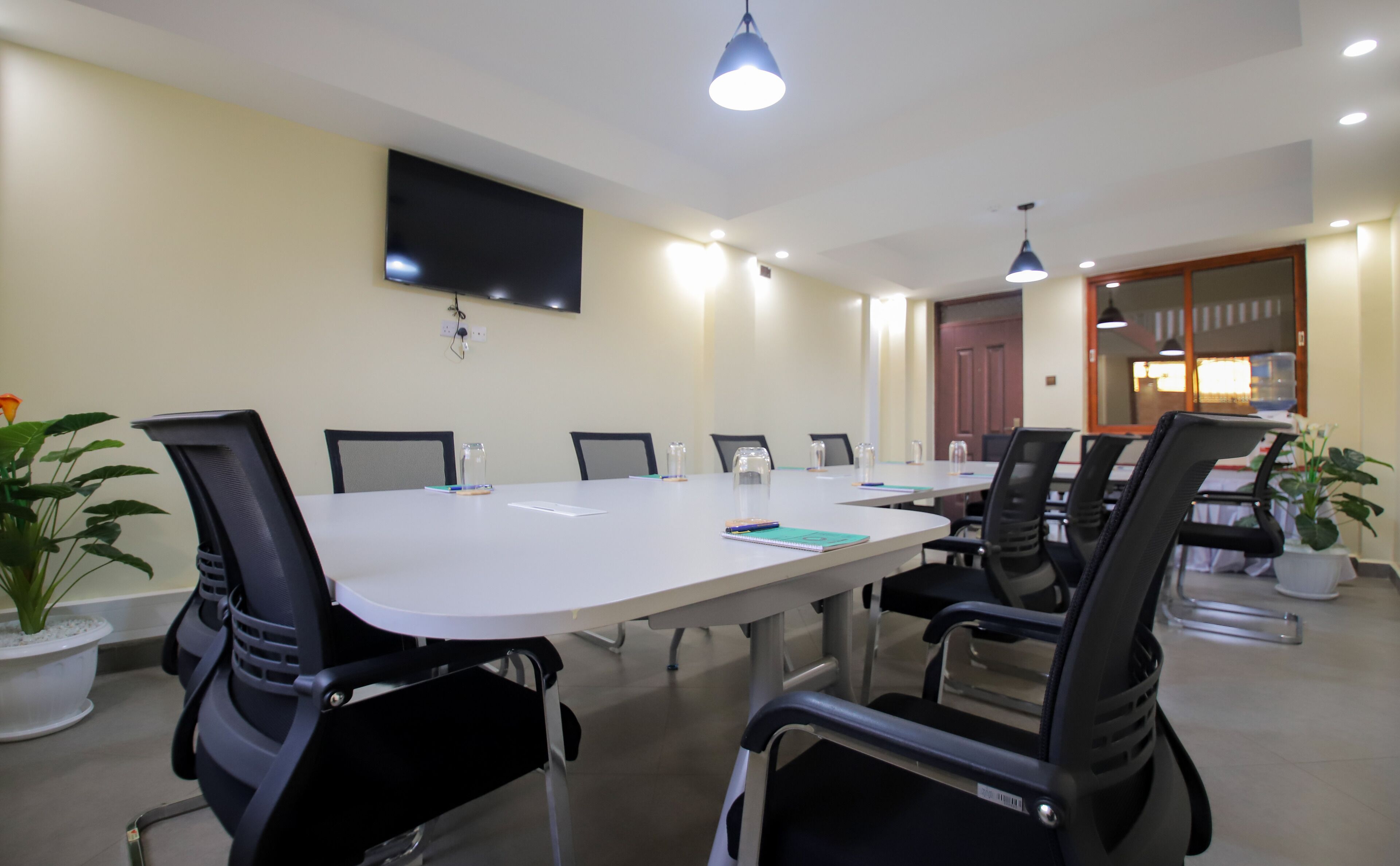 A conference room with a long table, black chairs, a flat-screen TV on the wall, and ceiling lights.