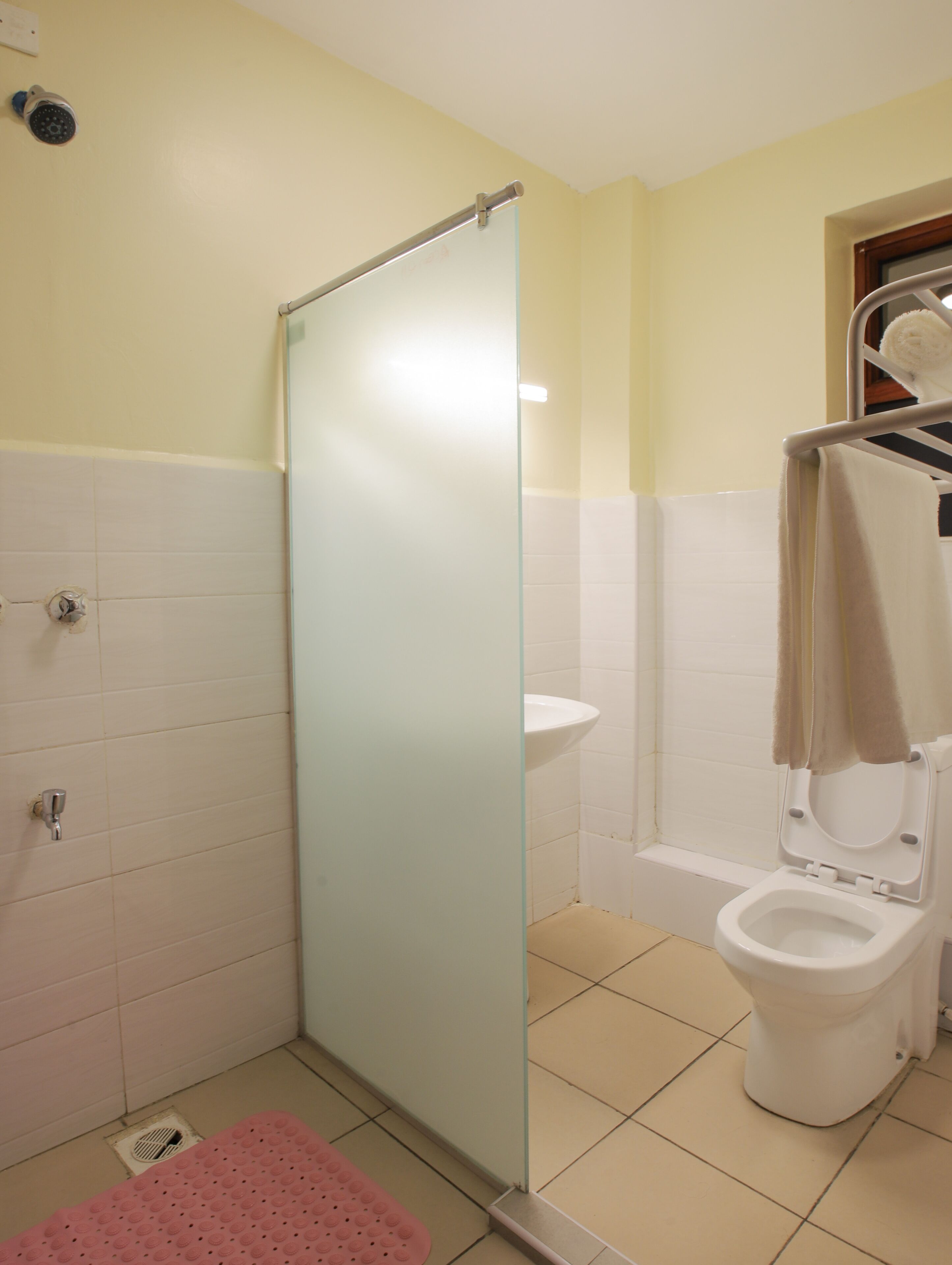 A bathroom with a glass shower enclosure, a white toilet, a sink, and a pink bath mat.