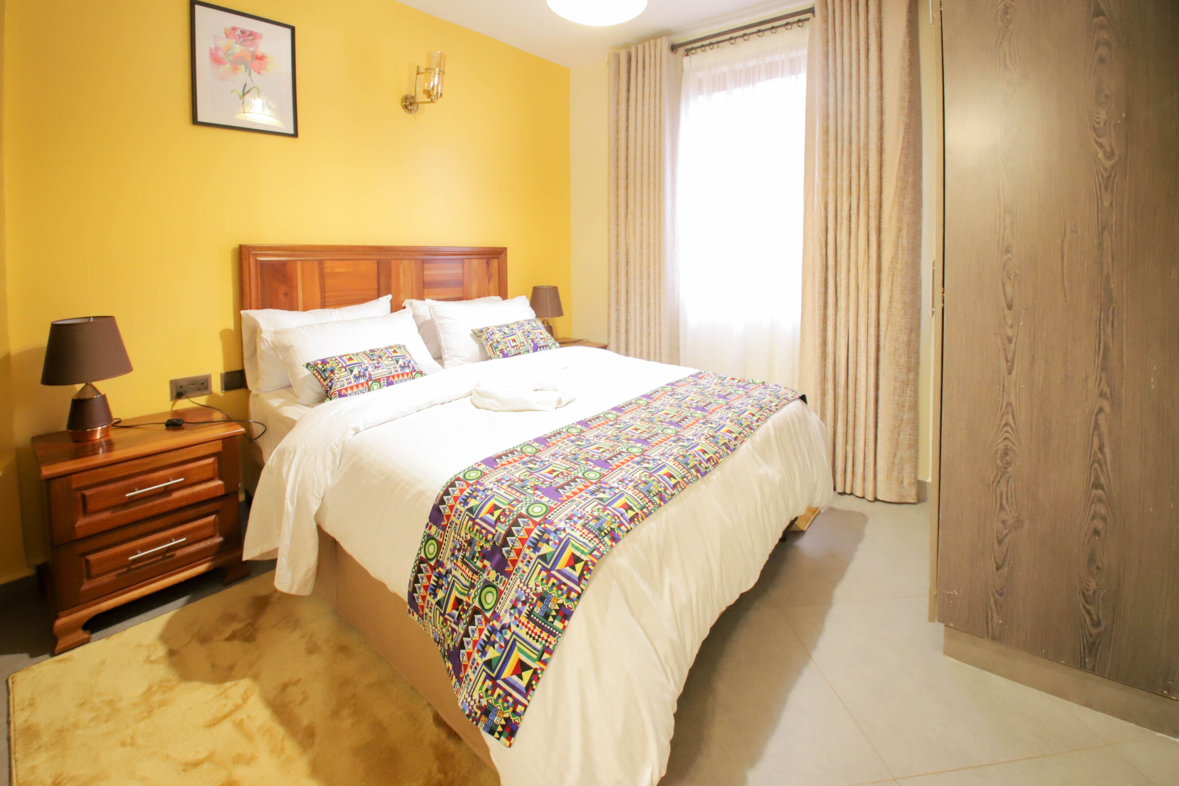 A hotel room with a bed, bedside tables, a lamp, a rug, a picture on the wall, and a window with curtains.