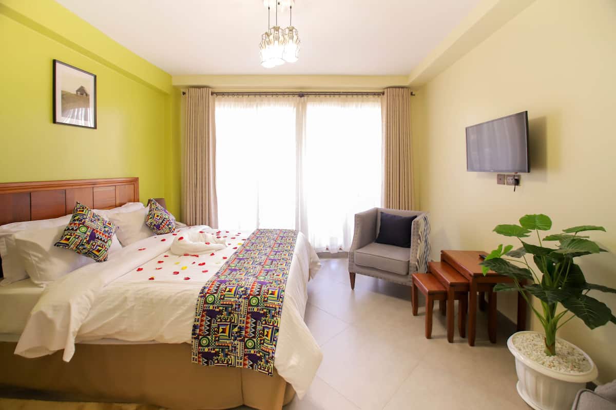 A hotel room with a bed, a desk, a chair, a television, and a potted plant.
