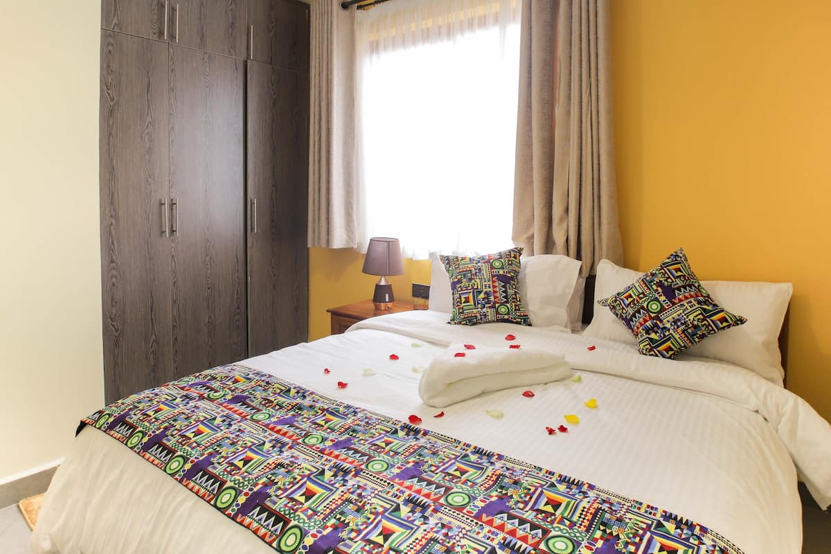 A hotel room with a bed, a nightstand, a lamp, and a window with curtains.