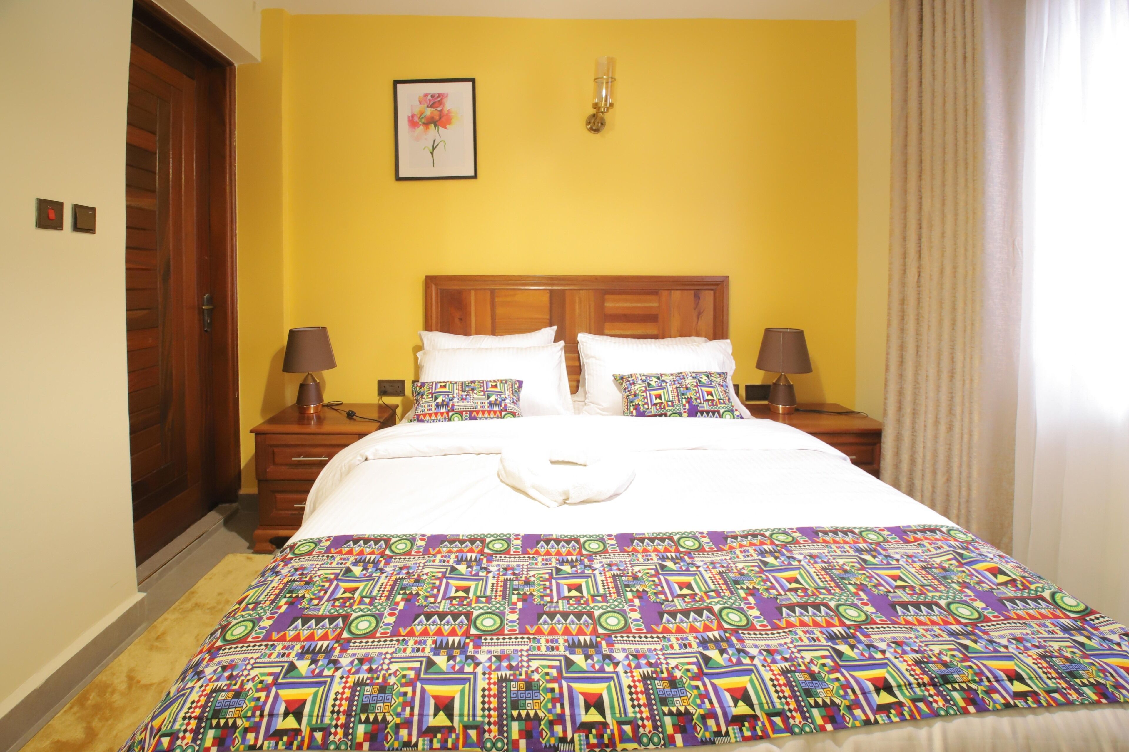 Una cama bien hecha con un edredón colorido, dos lámparas de noche y un cabecero de madera.