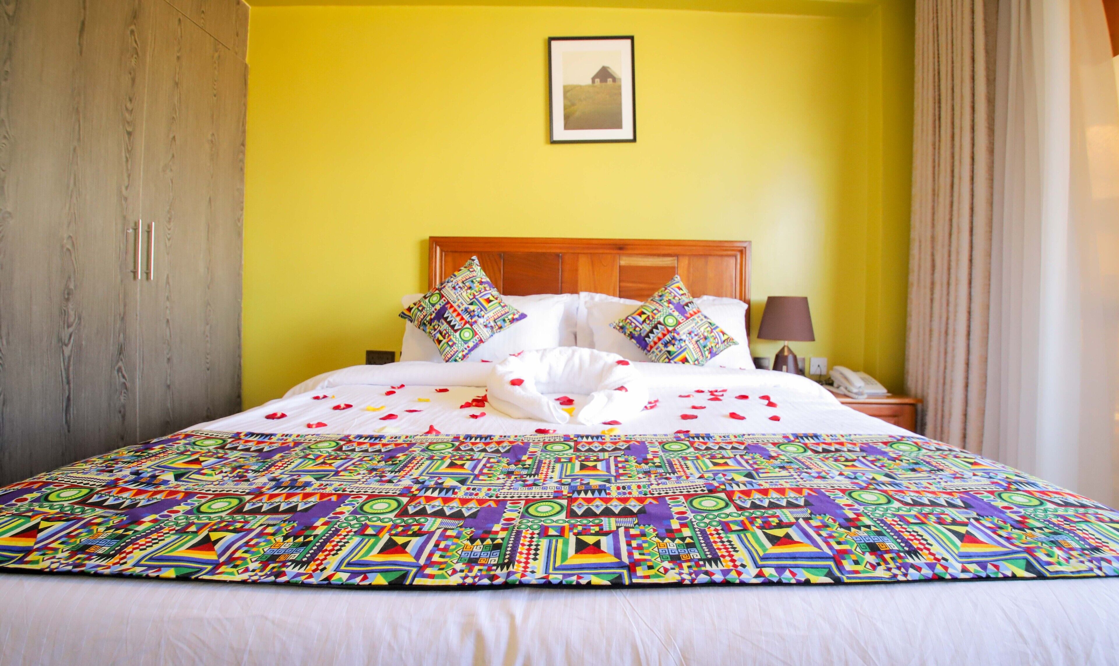 A bed with a colorful quilt, a wooden headboard, and a bedside table with a lamp and phone.