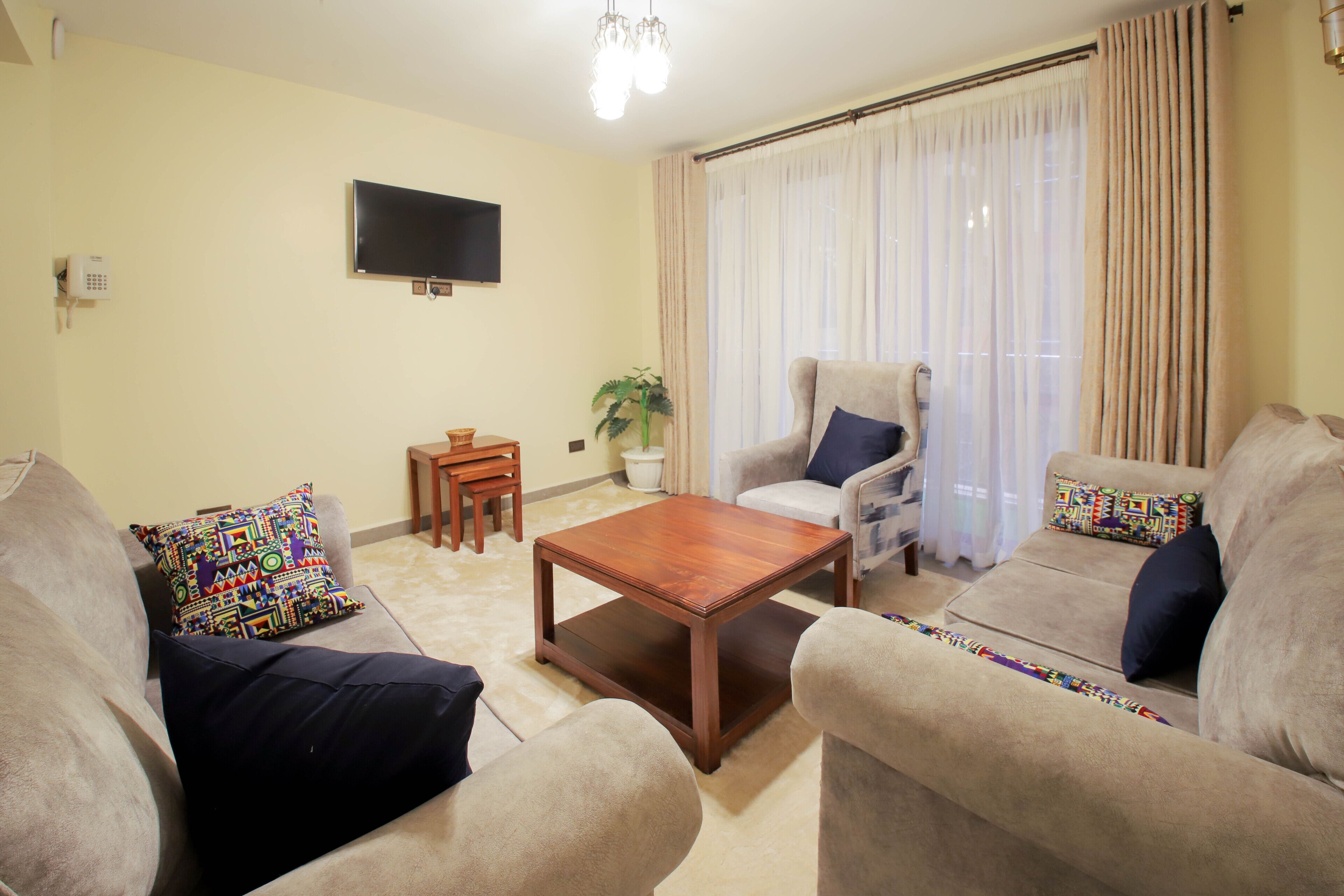 A living room with a sofa, armchair, coffee table, and a television on the wall.