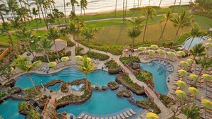 A resort with multiple swimming pools, palm trees, and a golf course in the background.