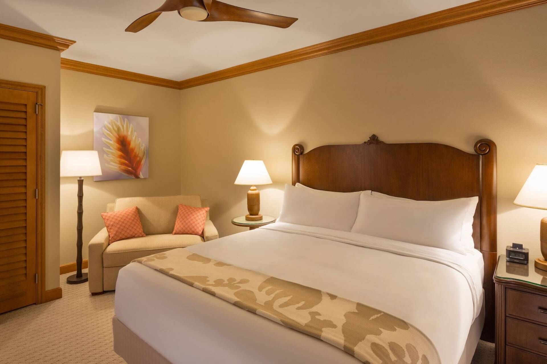 Una habitación de hotel con una cama grande, dos lámparas de noche, un cabecero de madera, suelo de madera y un ventilador de techo.