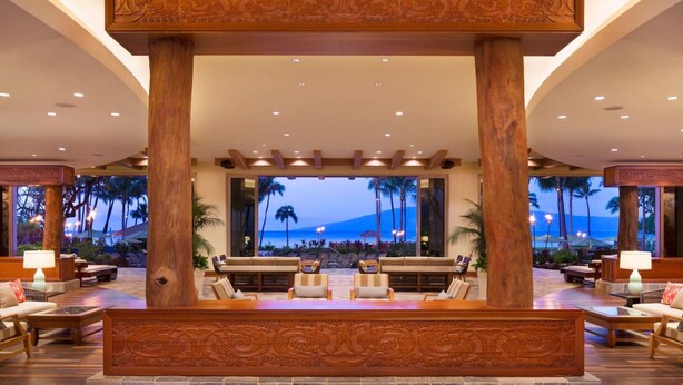 A lobby with a central seating area, large windows, and a view of palm trees and a beach.