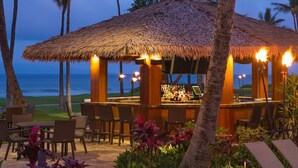 A thatched-roof bar area with outdoor seating, overlooking a beach.