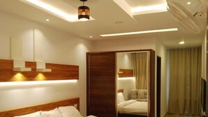 A modern hotel room with a large bed, bedside tables, a mirror, and a TV. - The Lavender Resort (Vythiri)