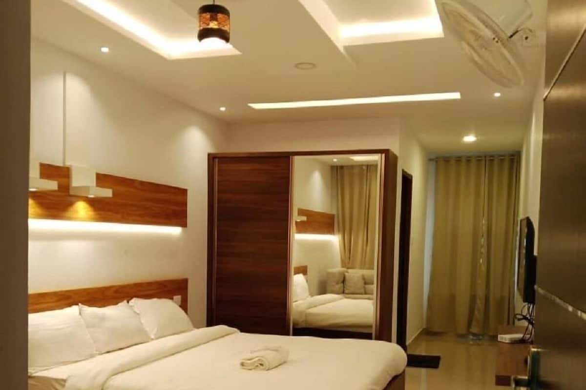 Ein modernes Hotelzimmer mit einem großen Bett, einem Kleiderschrank, einem Spiegel und einem Fernseher.