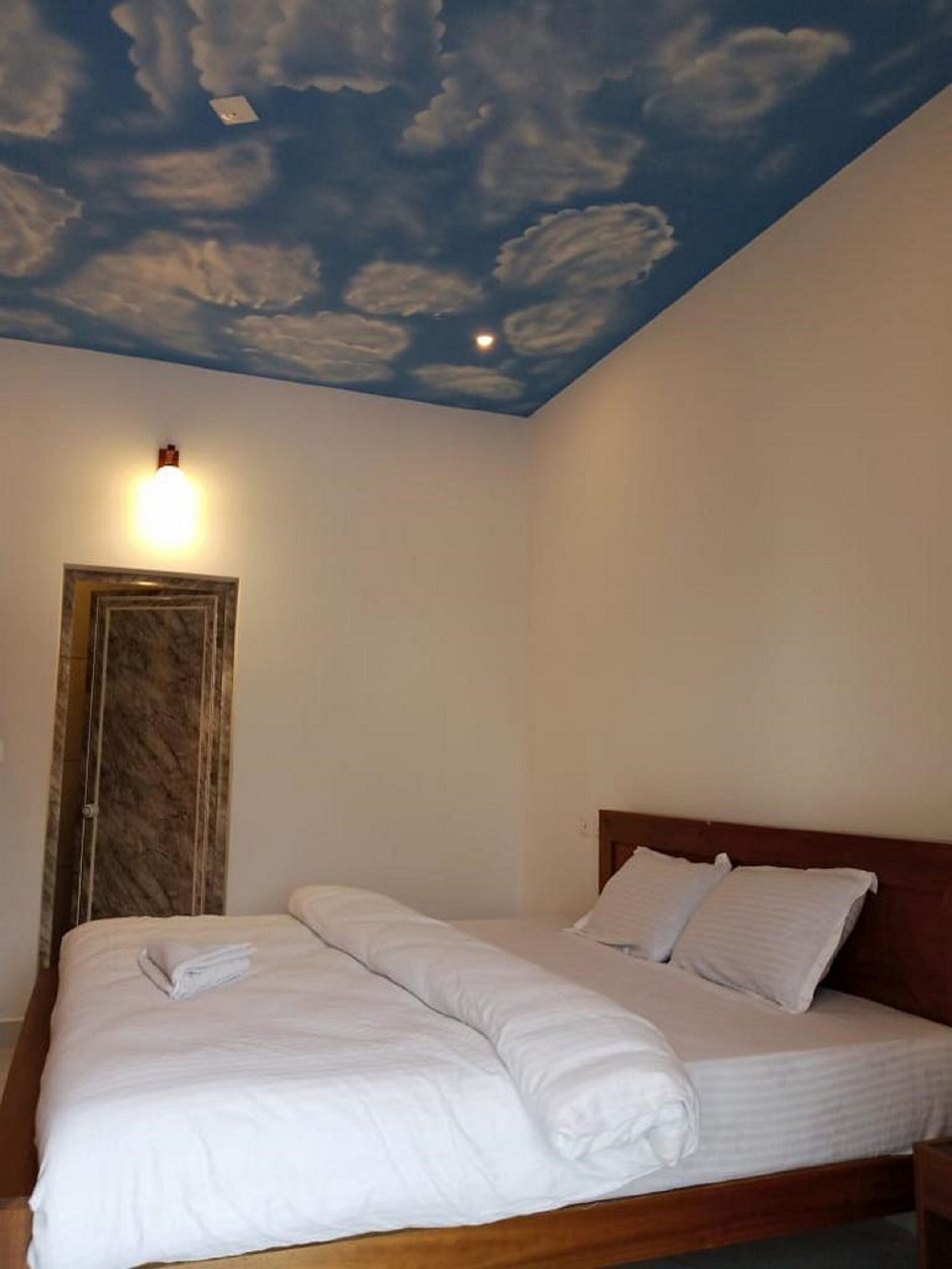 A bedroom with a bed, a door, and a ceiling painted to resemble a cloudy sky.