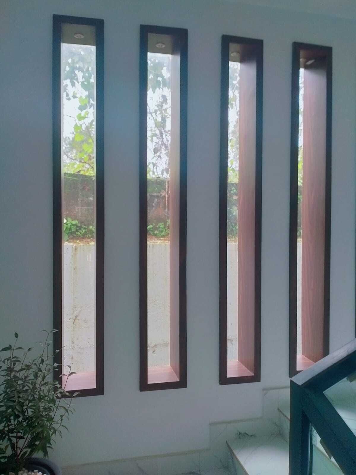 A room with three vertical windows with wooden frames, a potted plant, and a staircase leading to an upper level.