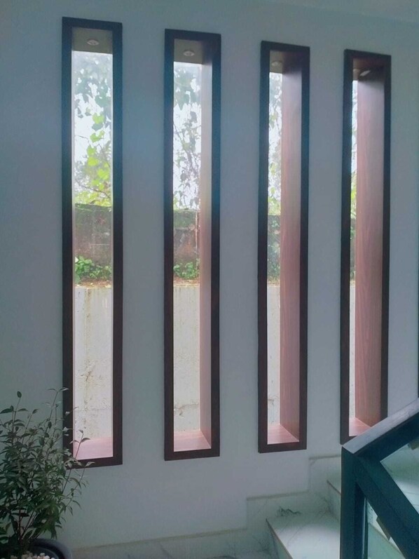 A room with three vertical windows with wooden frames, a potted plant, and a staircase leading to an upper level.