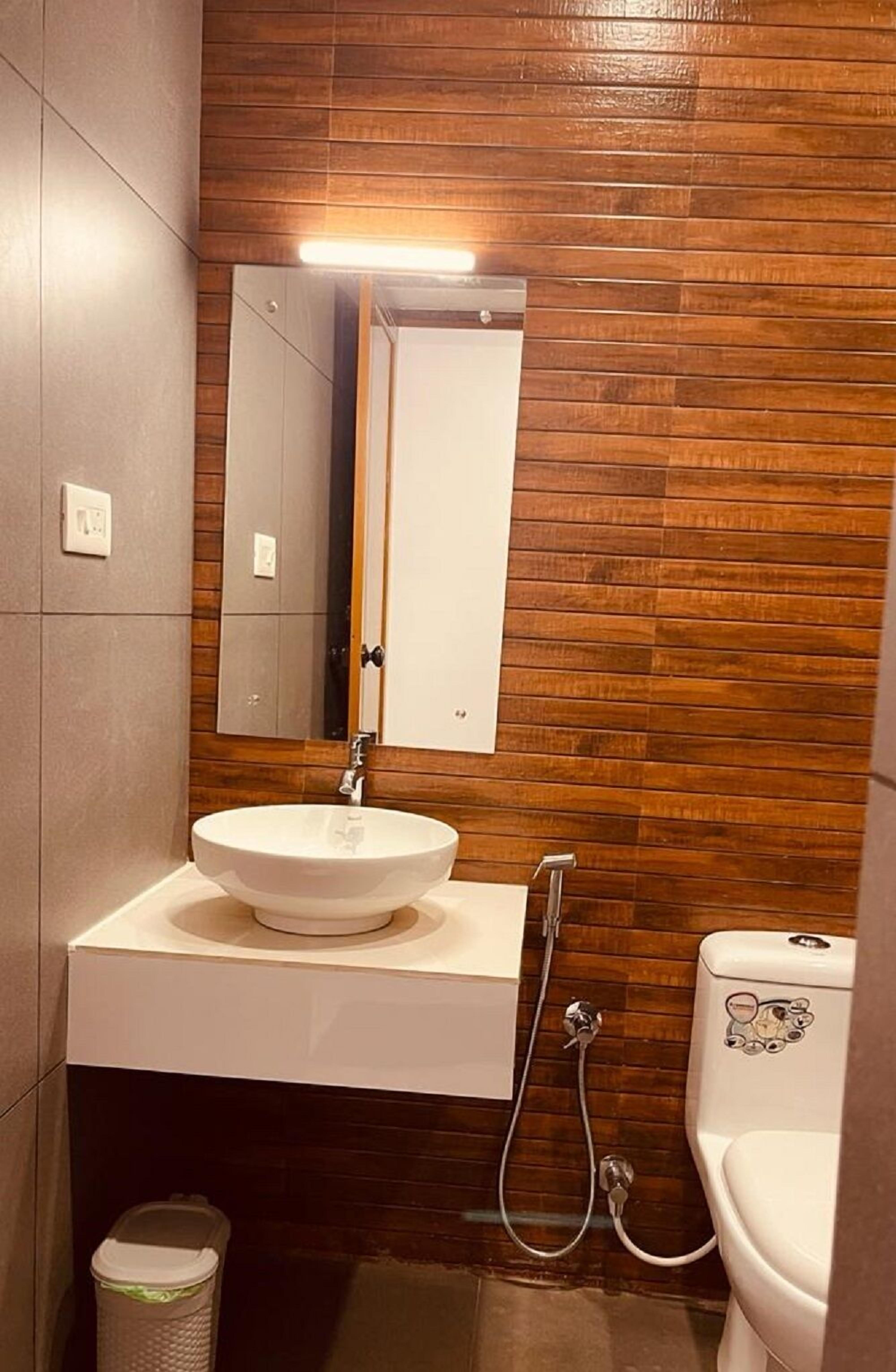 Un baño con pared de madera, un lavabo blanco, un espejo y un inodoro.