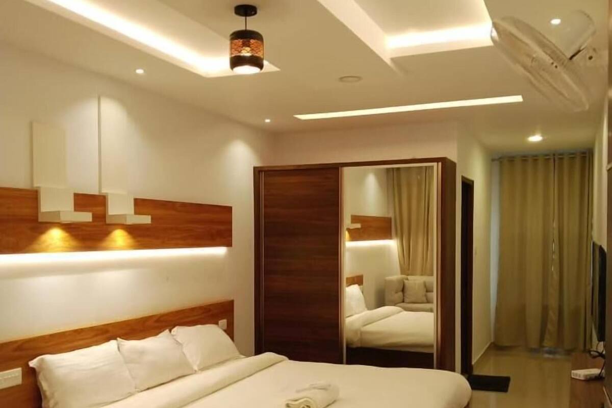 Ein modernes Hotelzimmer mit einem großen Bett, Nachttischen, einem Kleiderschrank und einem Spiegel.