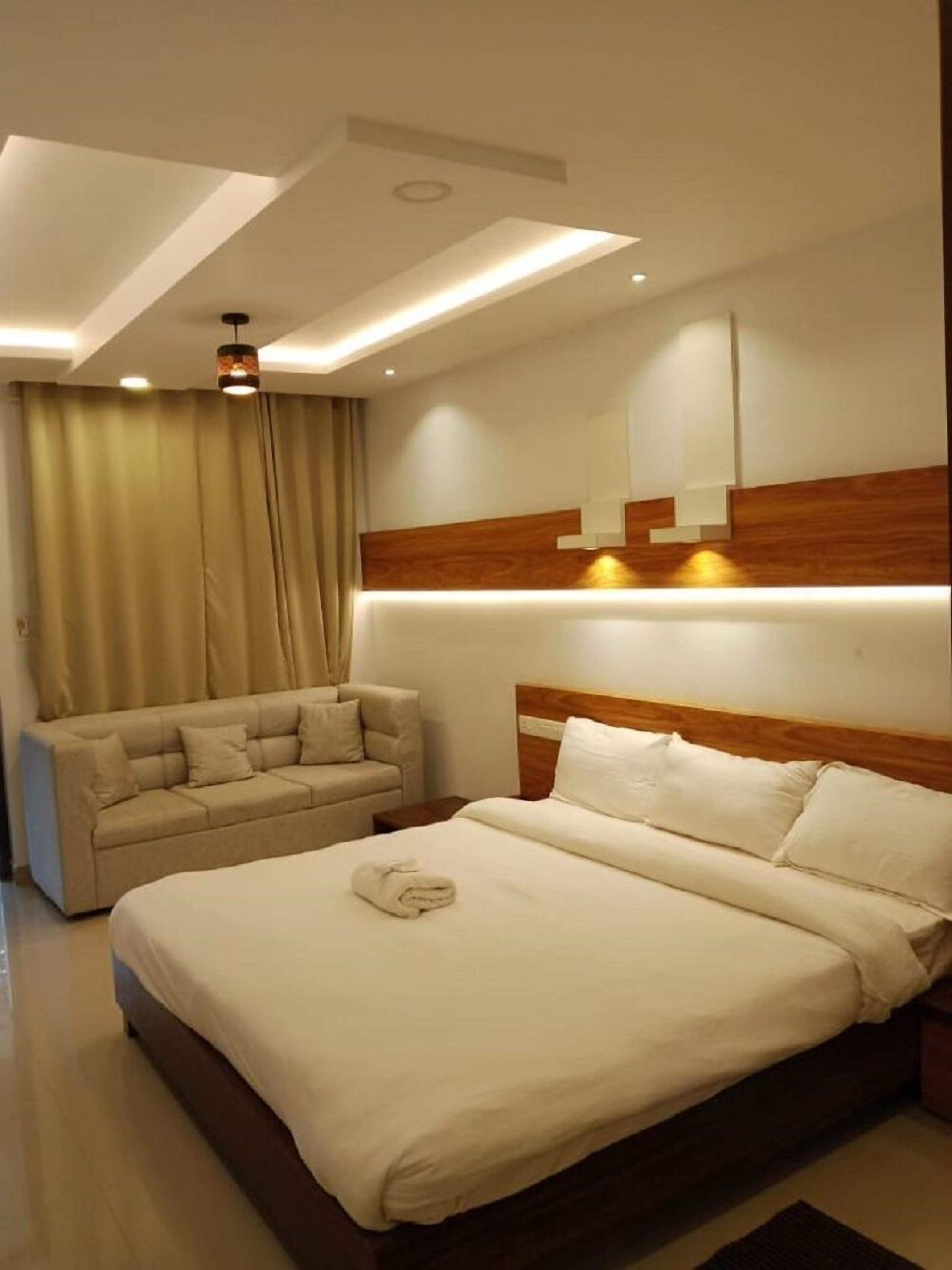A modern hotel room with a large bed, a sofa, and a ceiling light fixture.
