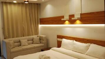 A modern hotel room with a large bed, a sofa, and a ceiling light fixture.