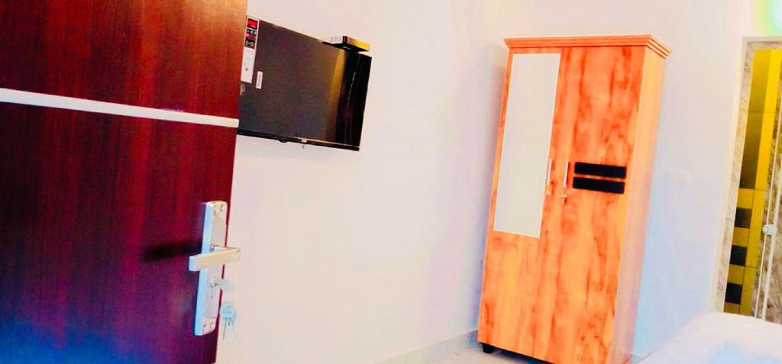 Una habitación con un armario de madera, un televisor montado en la pared y una puerta con manija.