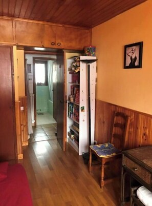 A narrow hallway with wooden flooring, a red carpet, a white cabinet with various items, and a chair with a patterned cushion. - Quiet mountain apartment with a beautiful view near the slopes   (Péone)