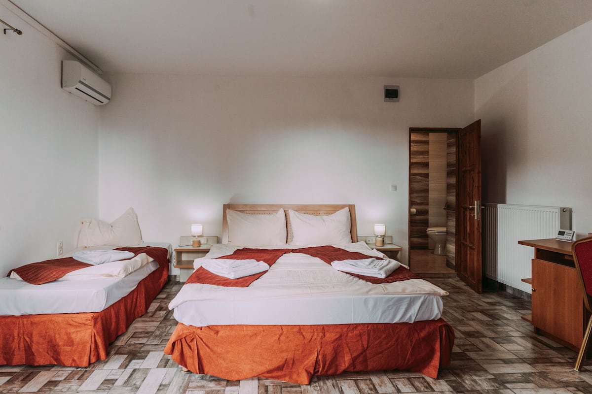 A hotel room with two beds, a wooden wardrobe, a desk, and a radiator.