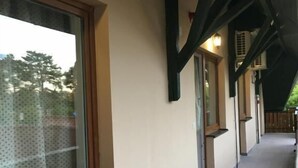 Un pasillo con ventanal de madera, techo con vigas a la vista y suelo de baldosas.