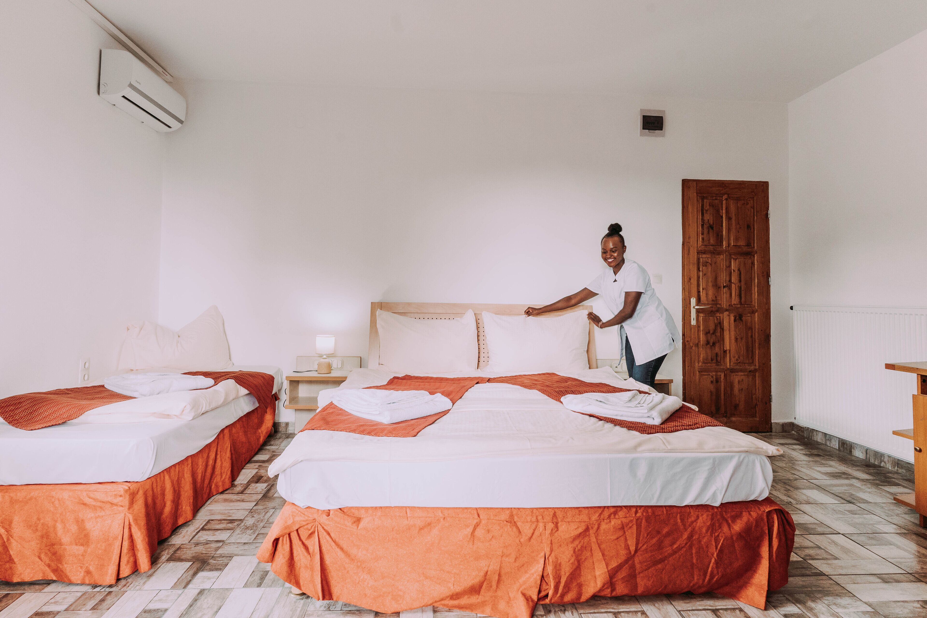 A hotel room with two beds, a wooden door, and a tiled floor.